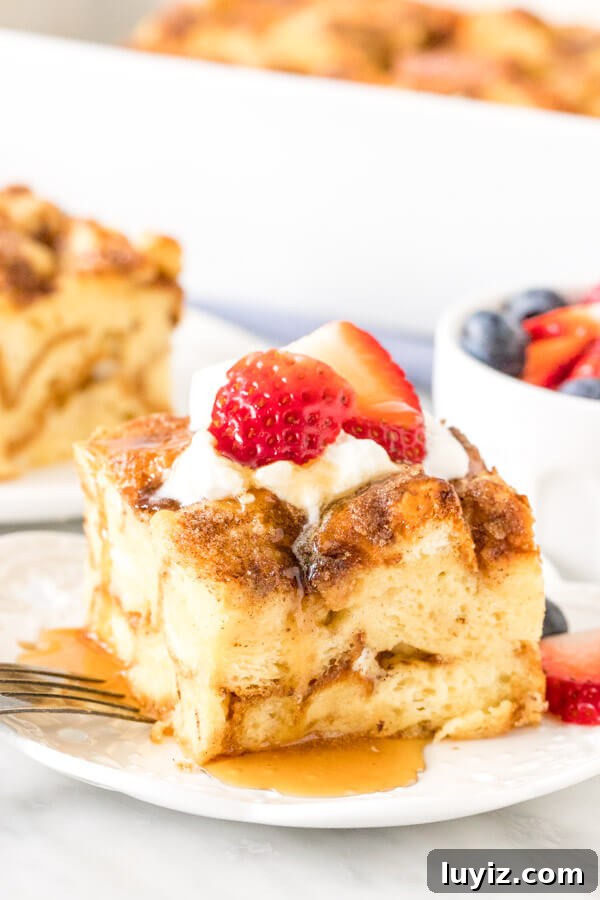 Make-Ahead French Toast Casserole for Brunch or Holiday Mornings 2 Slice of French toast casserole on a plate, topped with cream, berries and syrup.