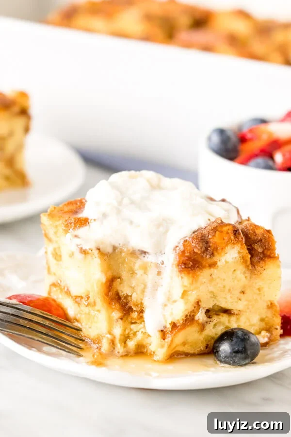 Make-Ahead French Toast Casserole for Brunch or Holiday Mornings 6 Square slice of french toast casserole with whipped cream on top and a bite taken out of it.