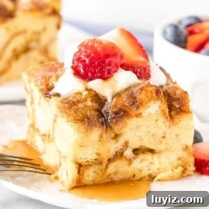 Slice of french toast bake with whipped cream, strawberries and maple syrup on top on a plate.
