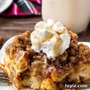 A slice of eggnog French toast bake with crumb topping, maple syrup and whipped cream.