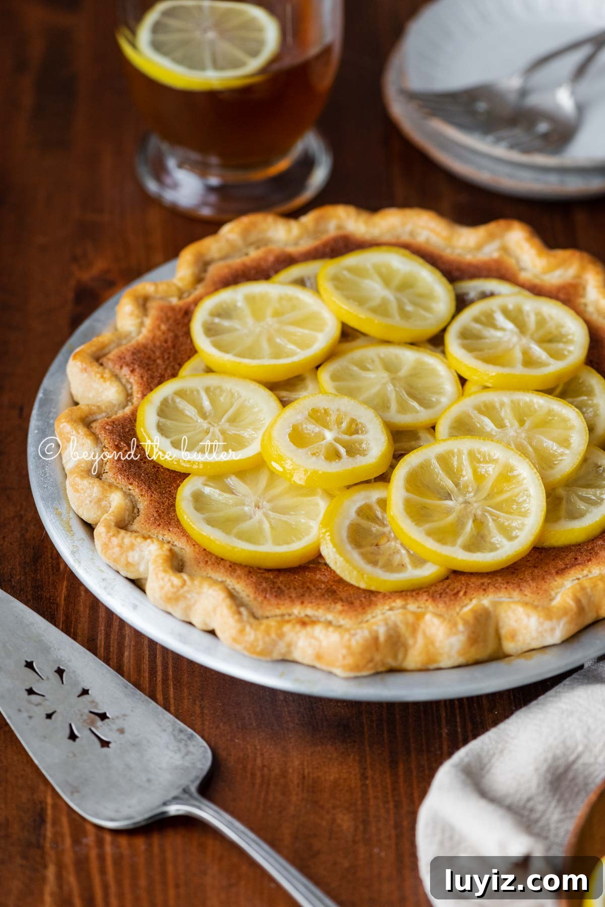 Classic Lemon Sponge Pie Recipe — Light, Zesty Dessert 7 lemon sponge pie on a dark wood dining room table with hot lemon tea | All images © Beyond the Butter®
