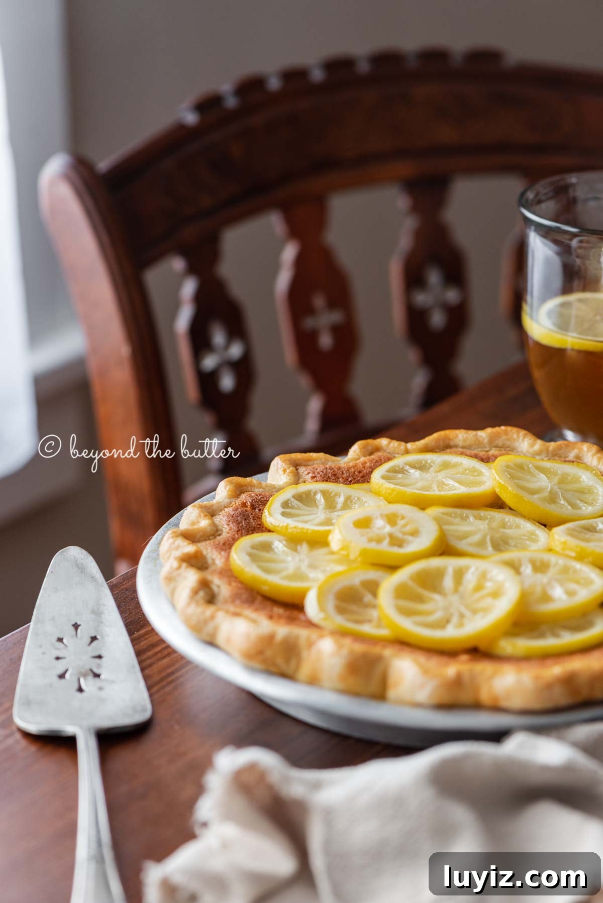 Classic Lemon Sponge Pie Recipe — Light, Zesty Dessert 8 lemon sponge pie on a dark wood dining room table with hot lemon tea | All images © Beyond the Butter®