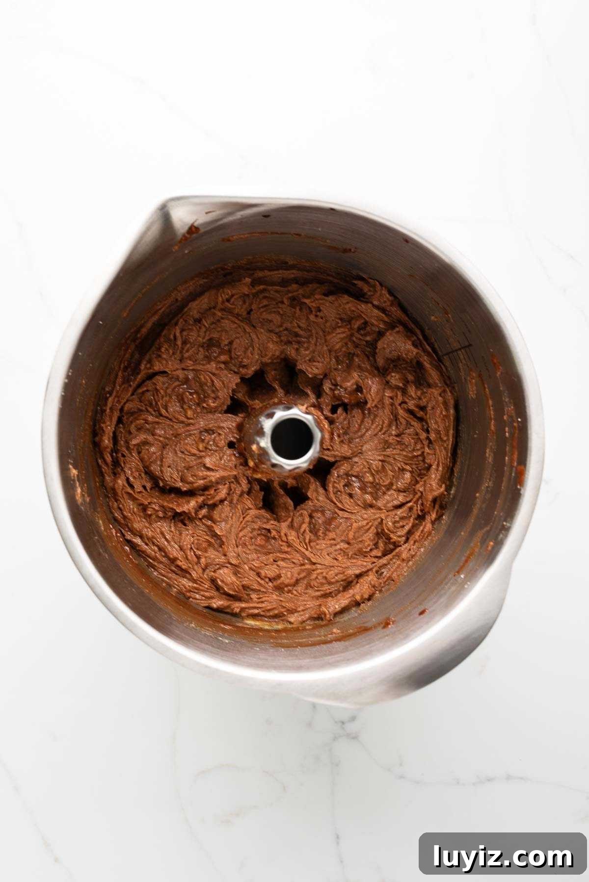 Melted chocolate and vanilla extract mixed into the cake batter in a stainless steel mixing bowl on a white marbled background.