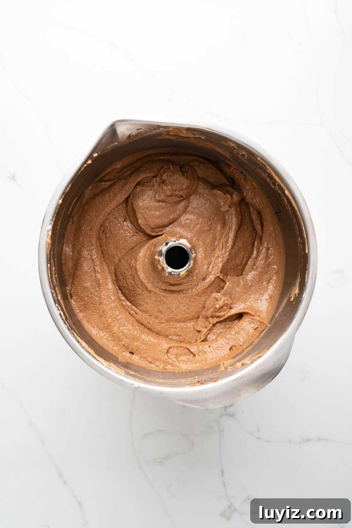 Stiff peak egg whites folded into German chocolate cake batter in a stainless steel mixing bowl on a white marbled background.