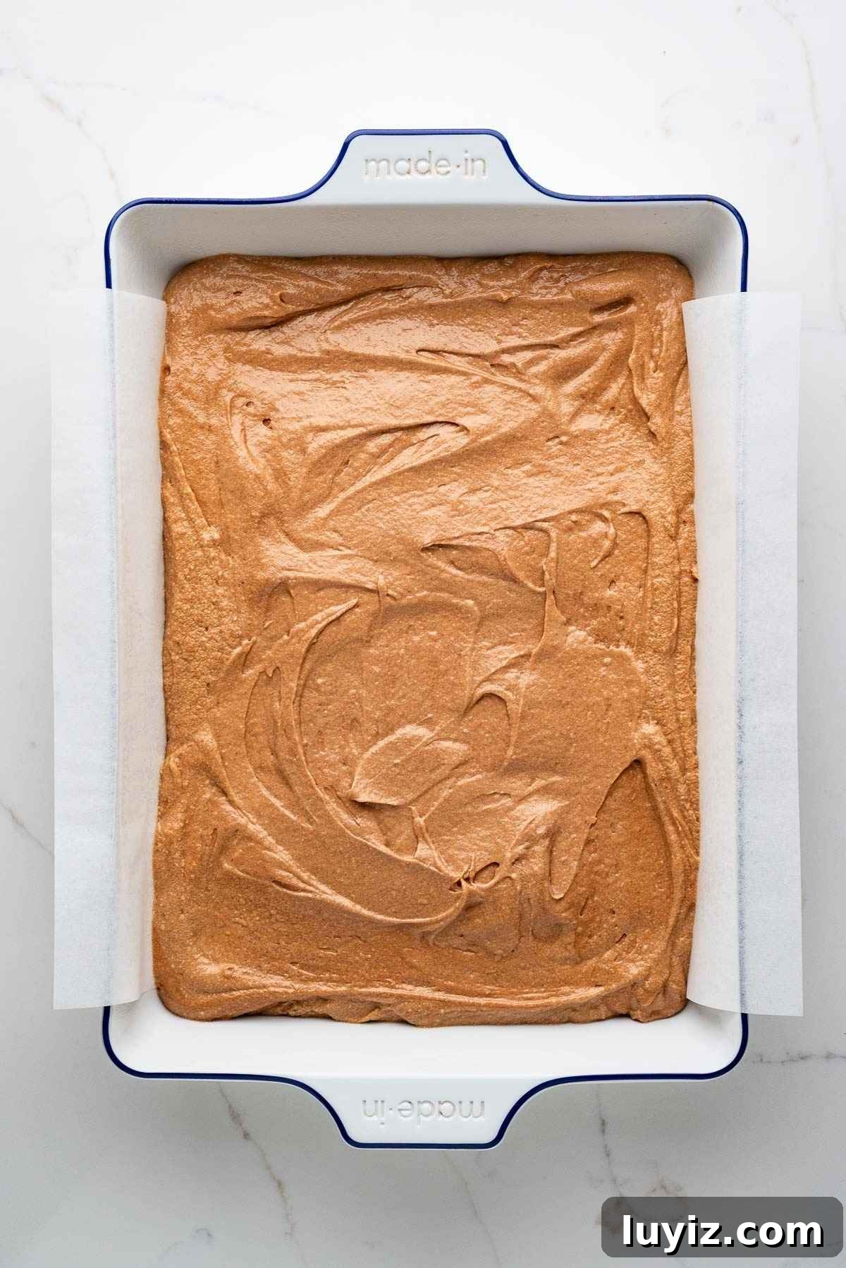 German chocolate cake batter spread into a parchment paper lined ceramic white baking dish.