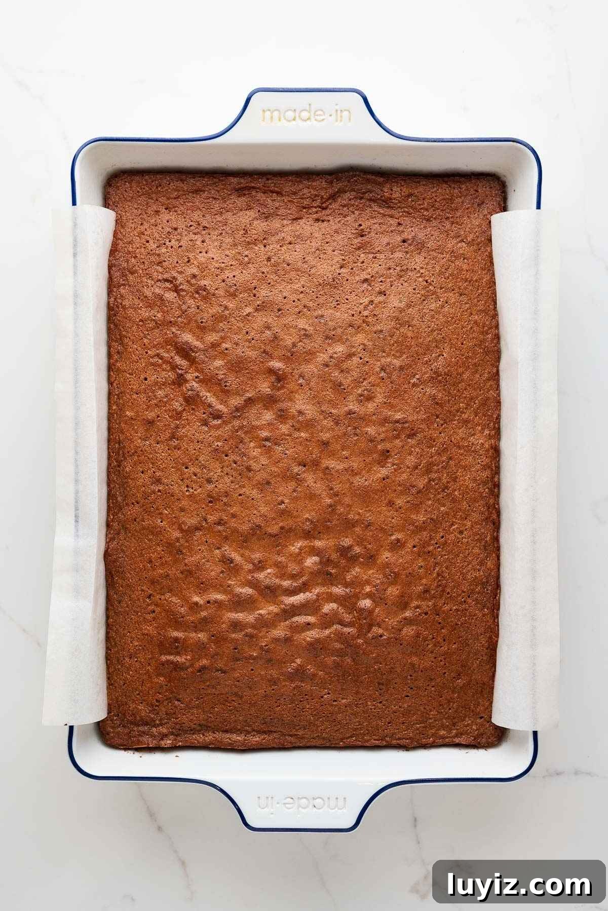 Baked German chocolate sheet cake in a parchment paper lined white ceramic baking dish.