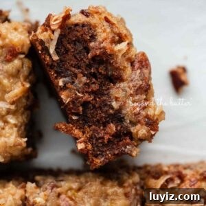 Sliced German chocolate sheet cake on its side next to other slices in a parchment paper lined ceramic baking pan.