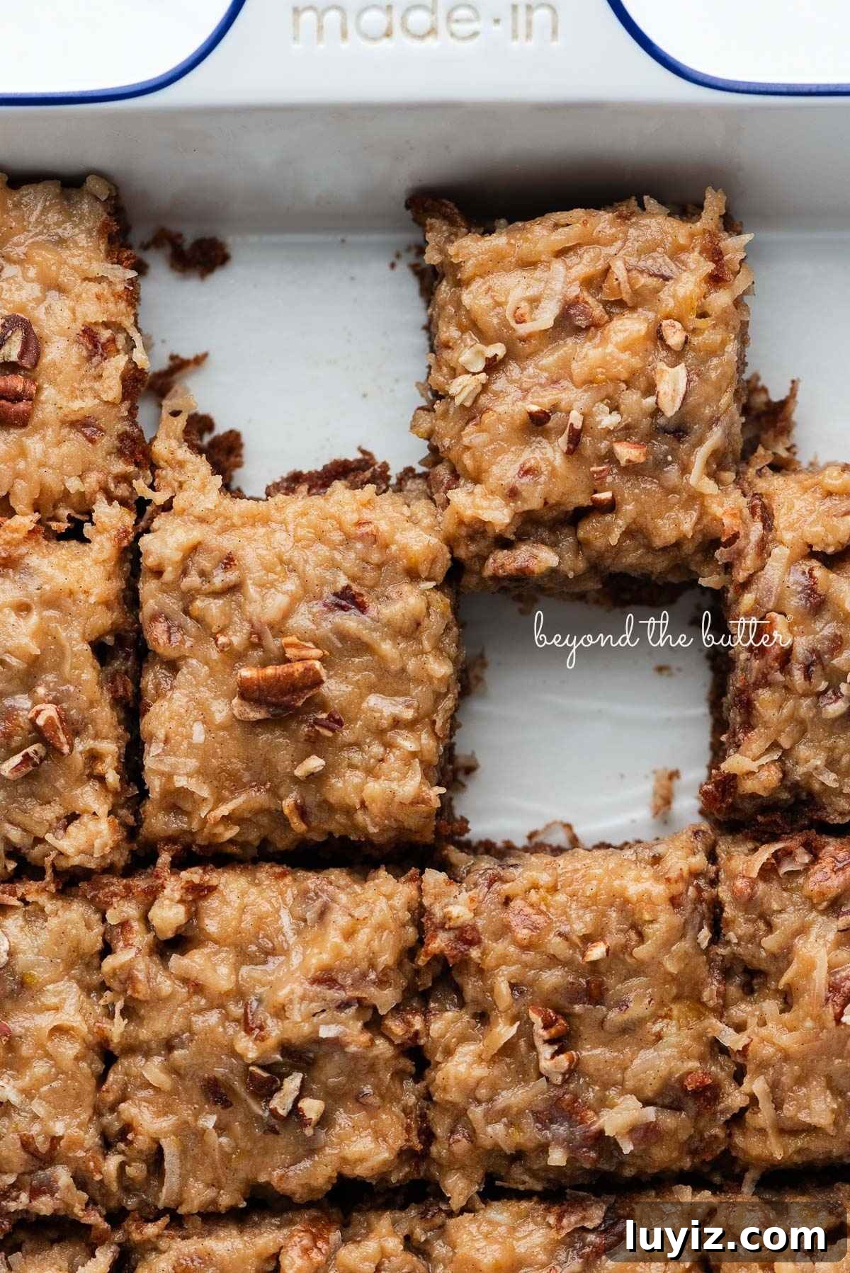 Slices of German chocolate cake in a parchment paper lined ceramic white baking dish.
