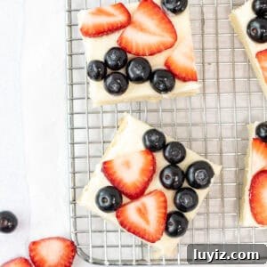 Berry-Topped Sugar Cookie Bars Recipe 6 Sugar cookie bars topped with vanilla frosting and fresh berries on a cooling rack