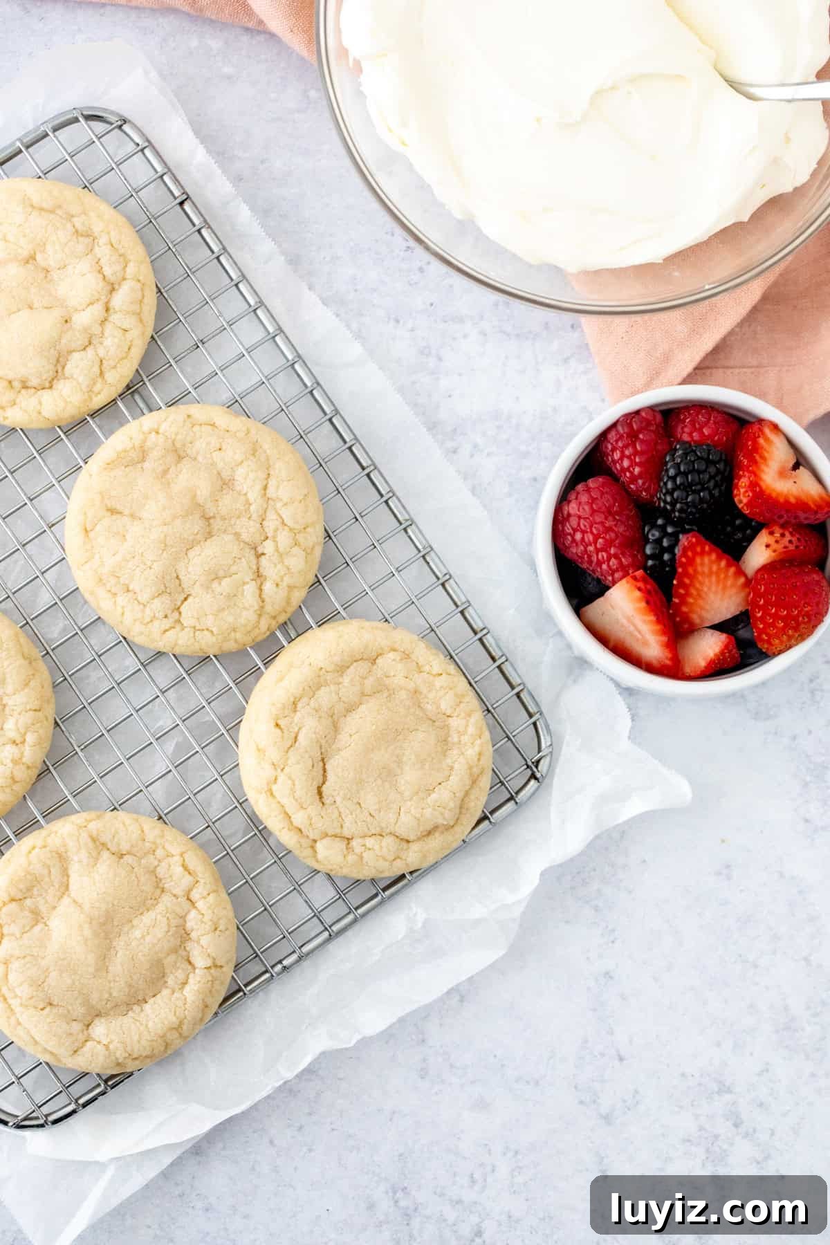 Mini Fruit Pizza Bites: Party Dessert Recipe 4 sugar cookies on wire rack with a bowl of whipped cream cheese frosting and berries