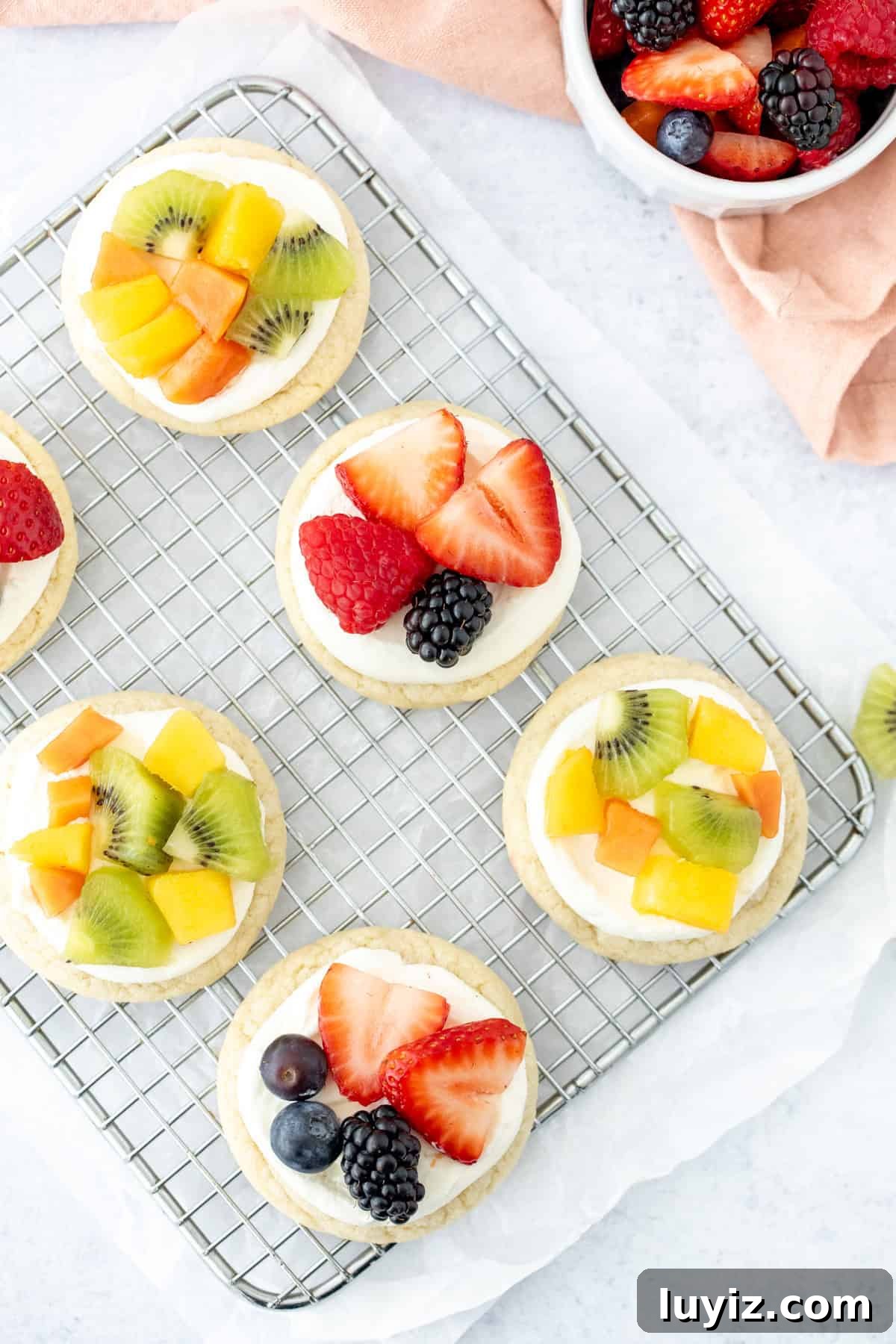 Mini Fruit Pizza Bites: Party Dessert Recipe 5 Mini fruit pizzas with cream cheese topping and fresh fruit on top, on a cooling rack