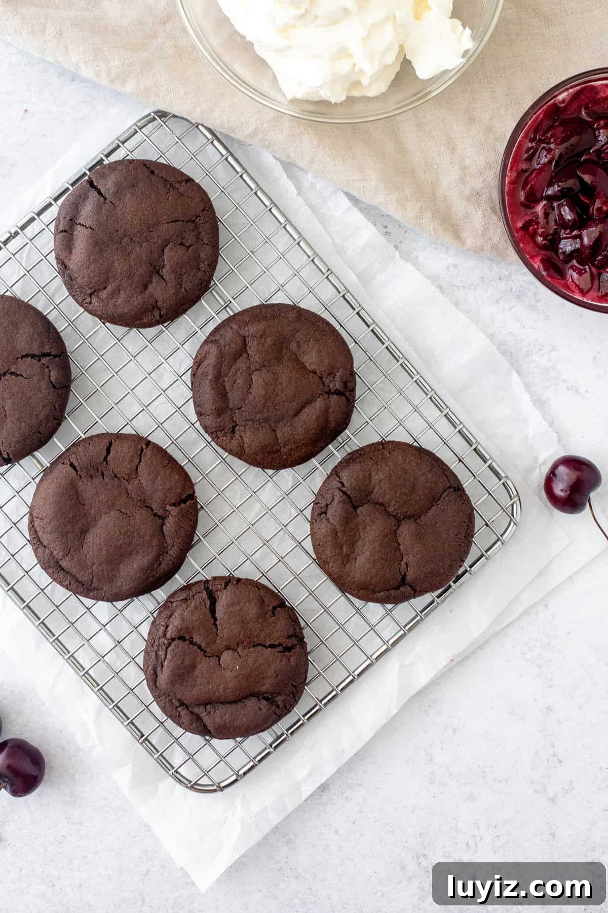 Black Forest Cherry Chocolate Cookies Recipe 5 chocolate cookies on a cooling rack with bowl of whipped cream and bowl of cherry sauce
