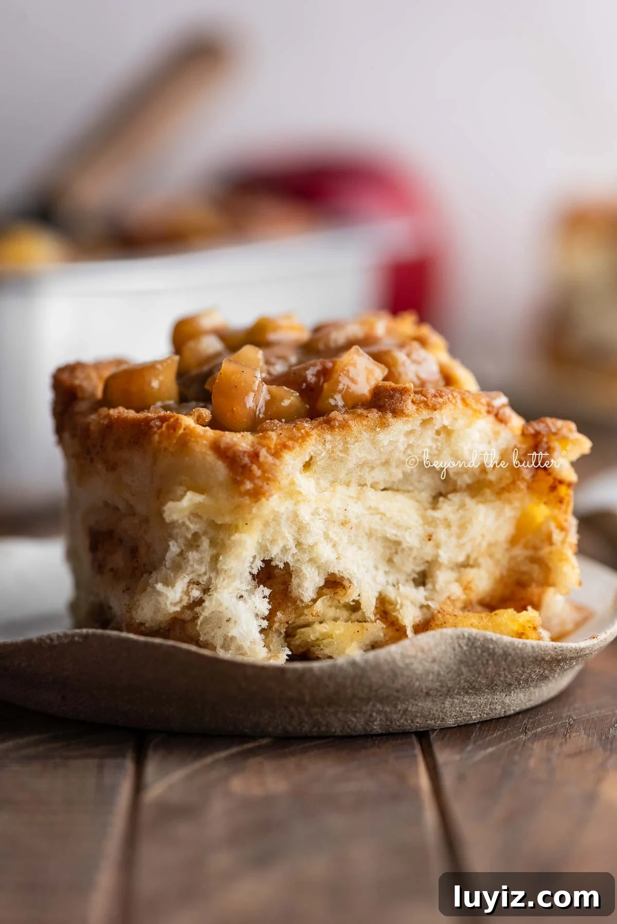 Apple streusel cinnamon roll on a ceramic dessert plate on a dark wood table with a pan of cinnamon rolls and apples in the background.