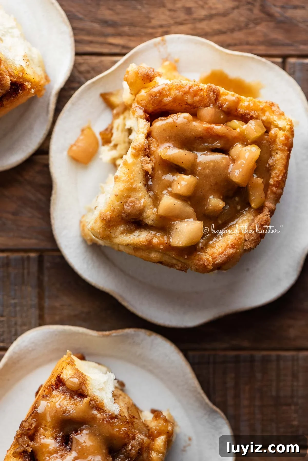 Apple cinnamon rolls topped with streusel and caramel glaze on plates.