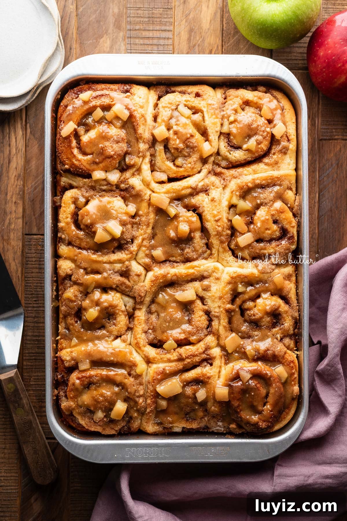 Pan of apple streusel cinnamon rolls topped with glaze on a table.